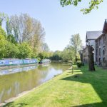 Canal boats and riverside homes on a sunny day.