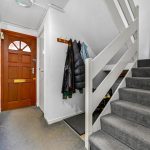 Hallway with wooden door, coats, and carpeted stairs.