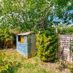 Garden shed with overgrown greenery and fencing.