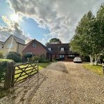 Countryside house with gravel driveway under cloudy sky.