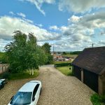 Rural view with farmhouse, trees, car and cloudy sky.