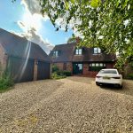 Brick house with car in gravel driveway, sunny day.