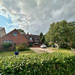Red brick house with garden and cloudy sky.