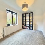 Empty room with window, bookcase, and grey carpet.