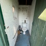 Small white brick outhouse with toilet and green door.