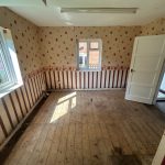 Empty room with patterned wallpaper and wooden floorboards.