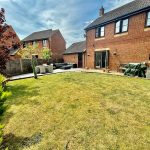Spacious garden with patio and red brick house.