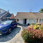 Blue car parked outside a bungalow with garden.