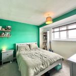 Cosy bedroom with green walls and wooden shelves.