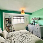 Cosy bedroom with green walls, bookshelf and dresser.