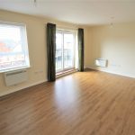 Spacious unfurnished room with wooden flooring and balcony.