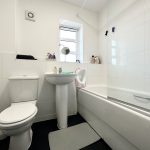 Clean white bathroom with toilet, sink, and bath.