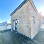 Sunny rooftop terrace with open door, clear sky.