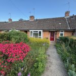 Brick bungalow with red door, garden path and flowers.