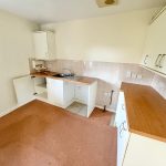 Empty kitchen with wooden countertops and white cabinets.