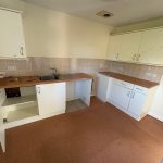 Empty kitchen with brown countertops and white cabinets.