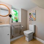 Modern bathroom with toilet, sink, mirror and artwork.