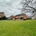 Spacious backyard with brick house, cloudy sky.