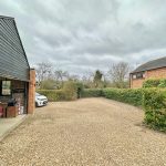 Gravel driveway with cars and greenery.