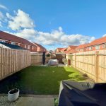 Sunny garden with fences and houses in background.