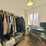 Small home office with clothes rack and desk.