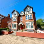 Victorian-style brick house with garden in sunlight.