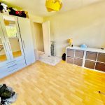 Bright bedroom with wardrobes, drawers, and ironing board.