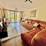 Spacious living room with large brown sofa, bright window.