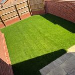 Sunny garden with grass and brick walls.