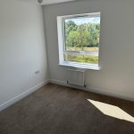 Empty room with window, beige carpet, outside view.