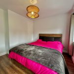 Bright bedroom with wooden floor and colourful bedding.