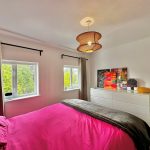 Bright bedroom with colourful paintings and wicker lampshade.
