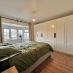 Modern bedroom with green bedding and white wardrobes.
