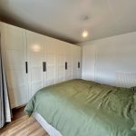 Modern bedroom with green bedding and white wardrobes.