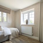 Modern bedroom with beige decor and large windows.