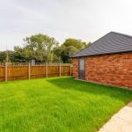 Sunny garden with green lawn and brick building.