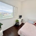 Minimalist bedroom with desk, bed, plant, and window view.