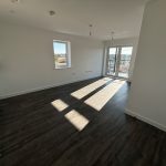 Empty apartment with wooden floors and large windows.