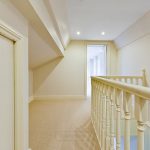 Carpeted hallway with white railing and recessed lights.