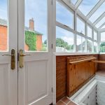 Bright sunroom with white doors and brick walls.