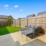 Private garden with patio furniture, wooden fence, sunny day.
