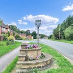 Village road with sign and flowers.