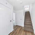 Bright hallway with carpeted stairs and wooden floor.