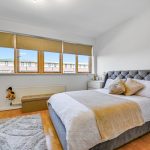 Modern bedroom with grey bed and large windows.