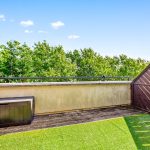 Sunny balcony with artificial grass and wooden fence.