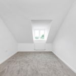 Bright empty attic room with carpet and window.