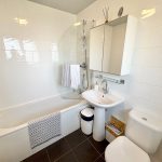 Modern white bathroom with bath, sink, and toilet.