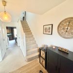 Modern hallway with stairs, clock, and decor.
