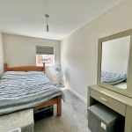 Small bedroom with bed, mirror and fan.