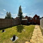 Sunny garden with grass, pathway, and wooden fence.